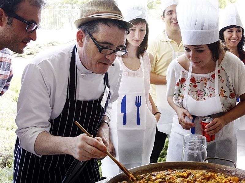 Cocinero enseñando a remover la paella a un grupo con delantales puestos