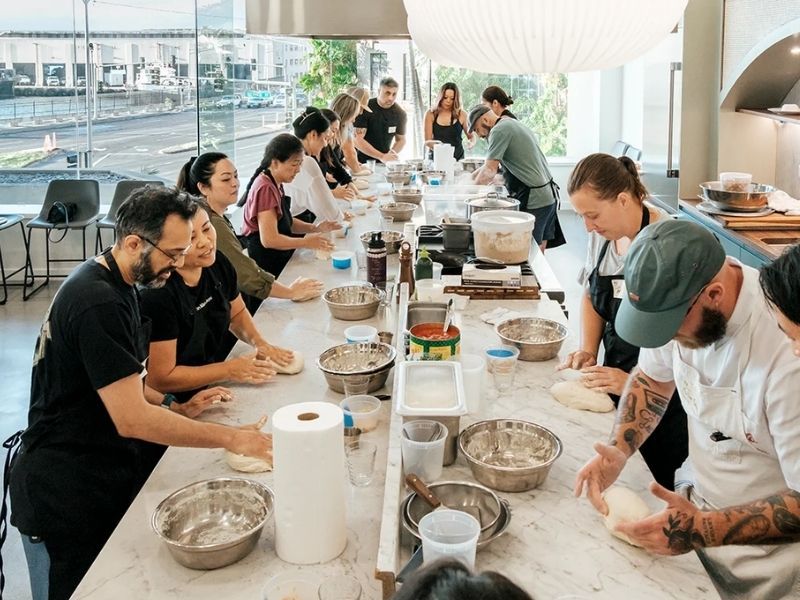 Plantilla amasando a lo largo de una mesa corrida con dos cocineros guiando