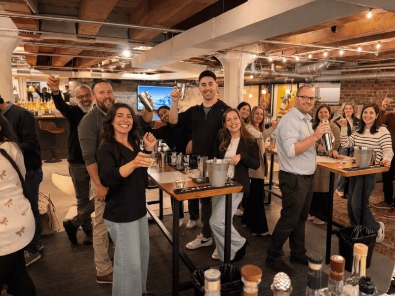 Grupo celebrando con las cocteleras en alto delante de una barra