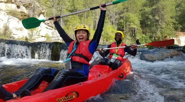 Dos personas bajando un rápido en piragua con casco y chaleco