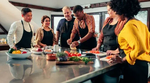 Grupo cocinando por parejas alrededor de una isla de acero