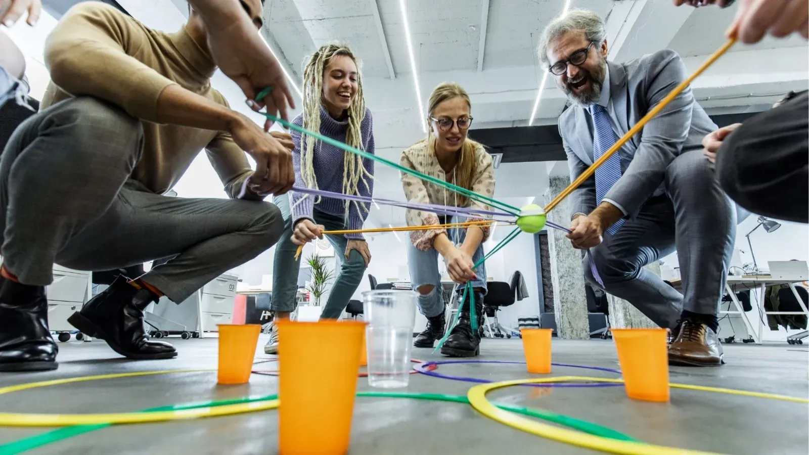Equipo manejando cuerdas para mover un vaso en una dinámica de oficina